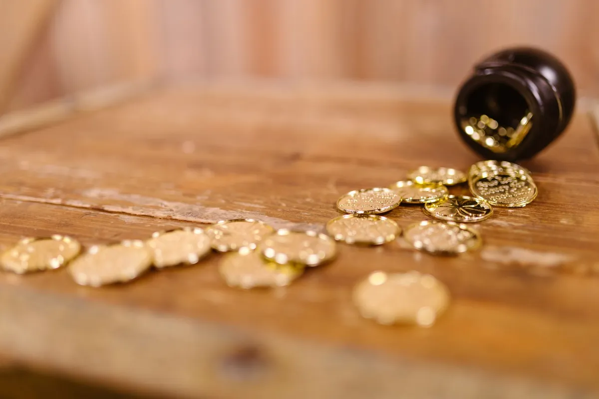 Des pièces d'or éparpillées sur une table en bois, échappées d'un petit pot renversé